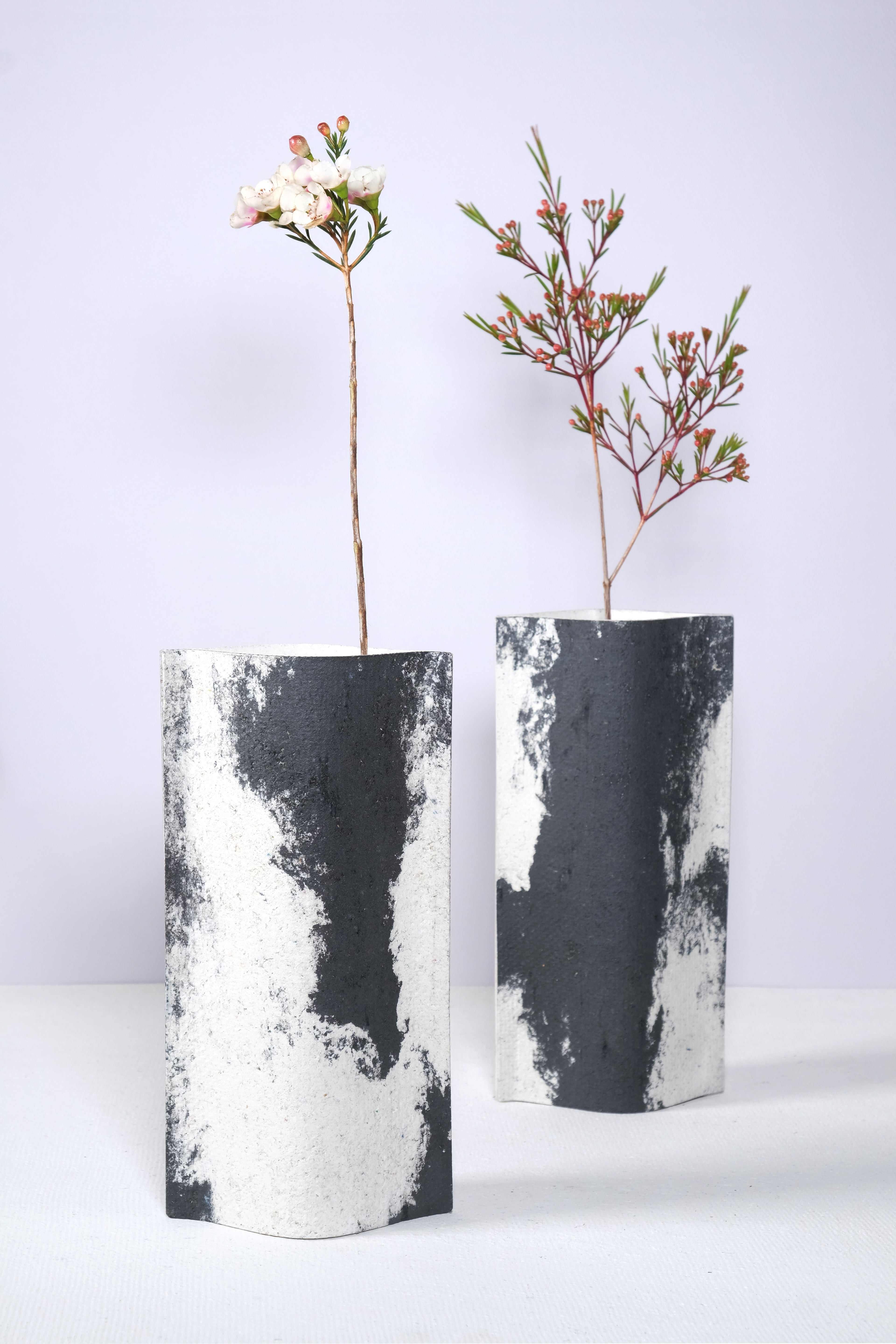 Duo de vases de la série ébène de profil rectangulaire sur fond blanc. Ces vases sont fabriqués à partir de deux feuilles de carton-pierre collées à leurs extrémités et ouvertes en leur centre pour y laisser passer un contenant étanche. Les vases arborent un effet marbré avec des veines couleur noir charbon sur fond blanc. Chaque vase a un marbré unique.